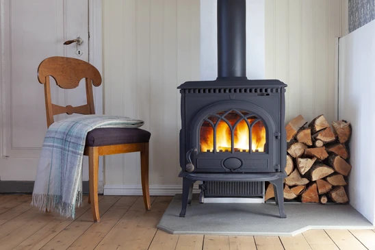 Intérieur avec poêle à bois en fonte noire allumé, flammes visibles à travers les vitres cintrées